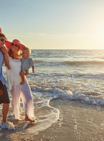 Happy family walks on the beach at sunset, smiles and waves in the background.