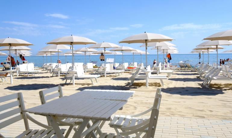 Spiaggia soleggiata, ombrelloni bianchi, relax e mare calmo all'orizzonte.