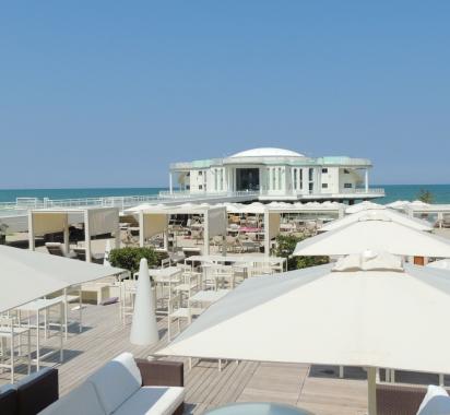 Spiaggia con ombrelloni bianchi e edificio sul mare in lontananza.