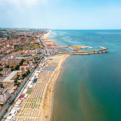 Vista aerea di una spiaggia con ombrelloni e mare calmo lungo la costa.