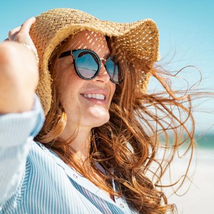 Donna sorridente con cappello di paglia e occhiali da sole in spiaggia.