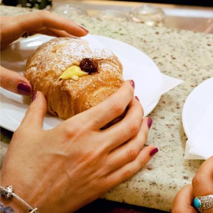 Mani femminili tengono un cornetto con crema e marmellata su piatto bianco.