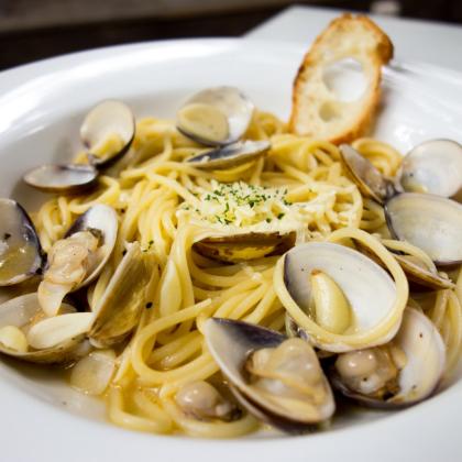 Spaghetti alle vongole con aglio e prezzemolo, serviti con crostino di pane.