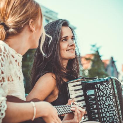 Due donne suonano strumenti musicali all'aperto, una fisarmonica e un ukulele.