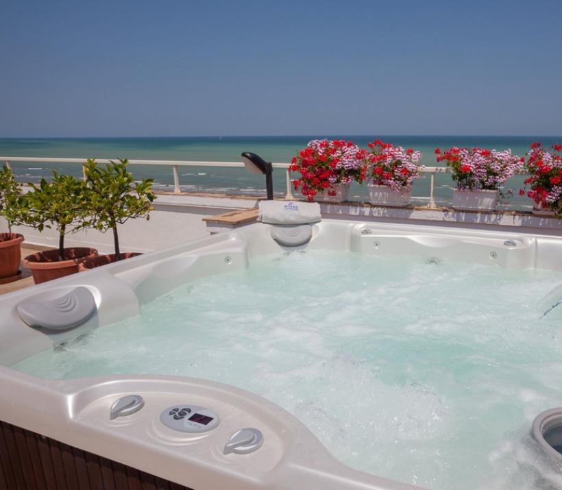 Vasca idromassaggio con vista mare, circondata da fiori colorati su una terrazza.