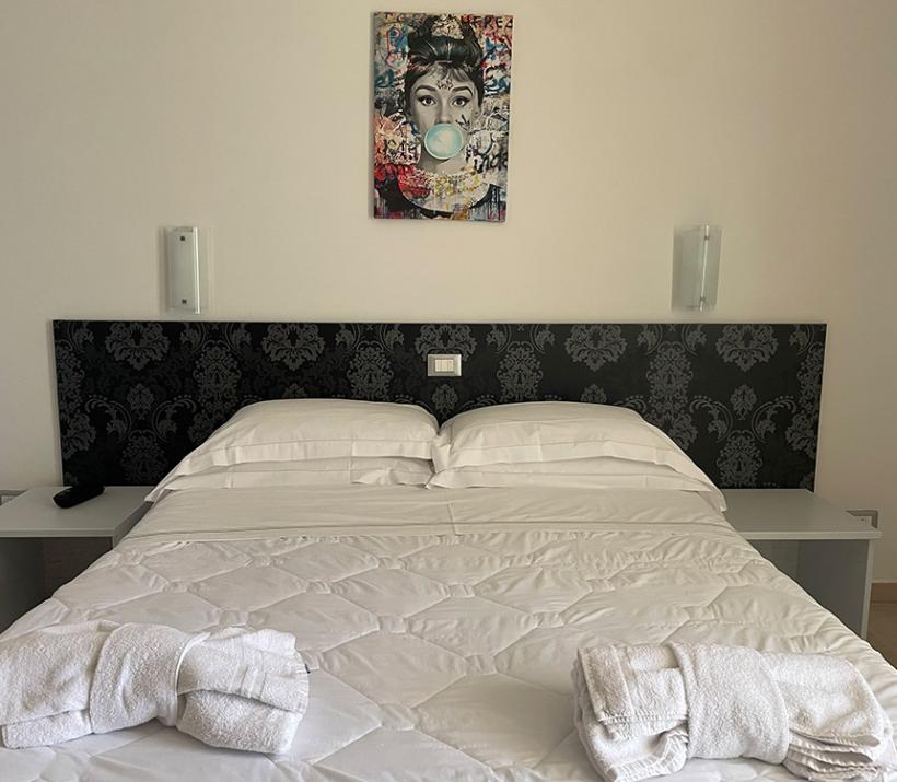 Camera con vista mare, letto bianco e quadro colorato.
